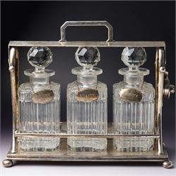 Early 20th century silver plated tantalus fitted with three square glass spirit decanters ...