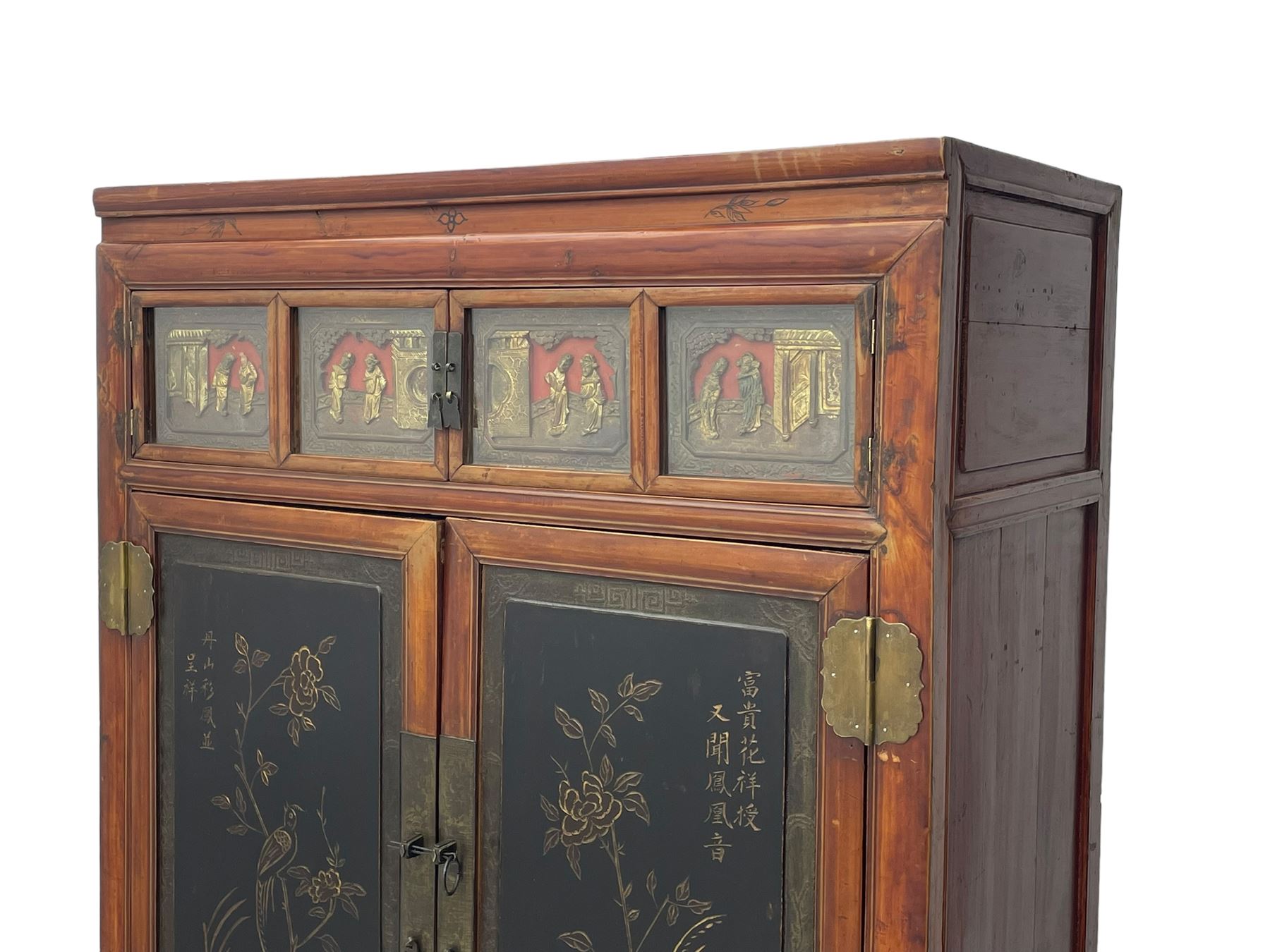 Late 19th century Chinese Qing dynasty red and black lacquered wood cabinet,  Fujianese province, upper cupboard enclosed by two doors with relief carved and gilt panels depicting figures behind glass, the large cupboard enclosed by two panelled doors carved with trailing foliate branches and birds, inscribed with Chinese characters, to the left ‘The red mountains are in the shape of Phoenixes and appear auspicious’ and to the right, ‘Wealth and honour are given by flowers and I hear the sound of the phoenix', fitted with two drawers, on square supports with carved brackets 