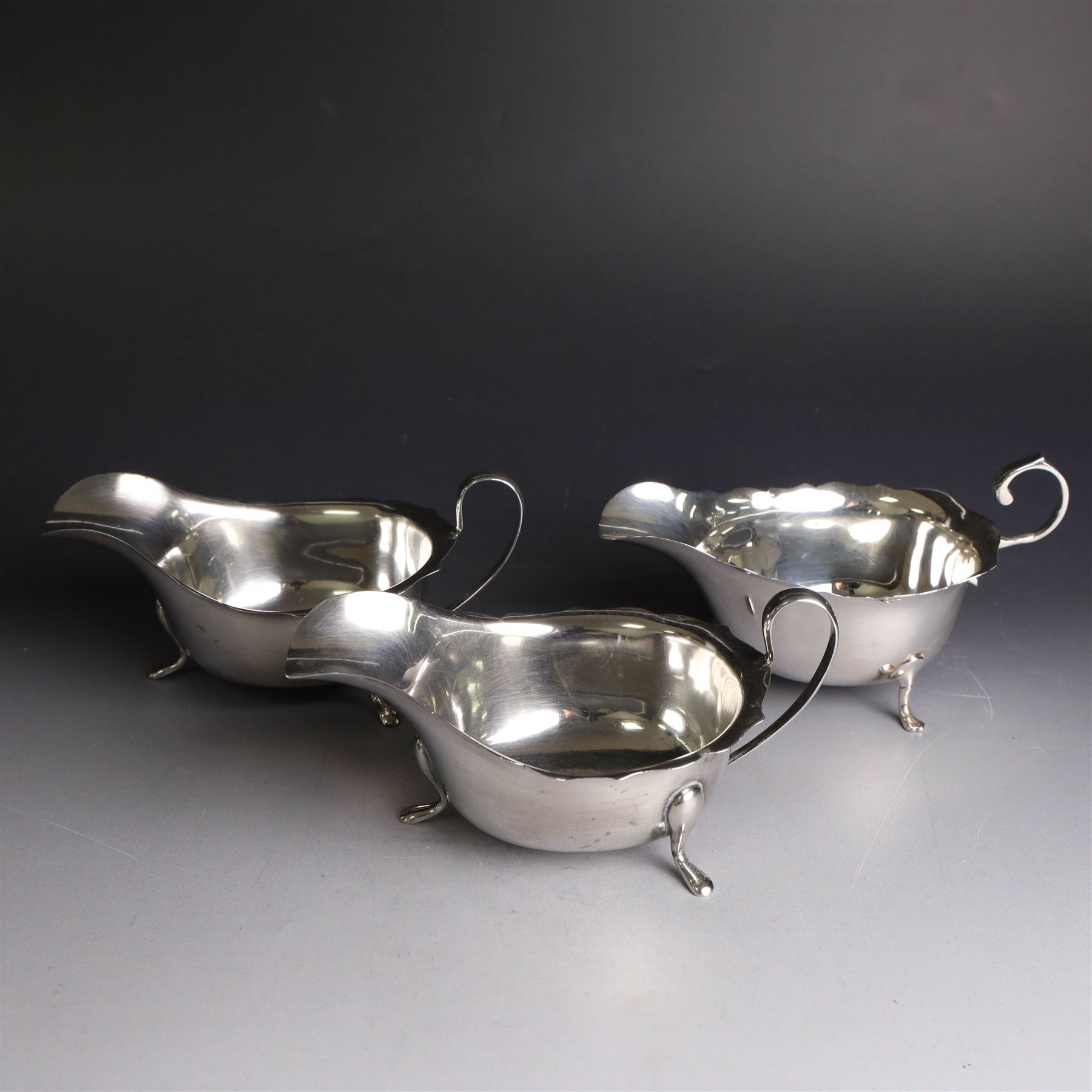 Three silver sauce boats, comprising pair of 1930s silver sauce boats, of typical form with shaped rim, scroll handle and upon three pad feet, hallmarked Viner's Ltd, Sheffield 1932 and a similar 1920s example with flying C scroll handle and upon three paw feet, hallmarked James Deakin & Sons, Sheffield 1923, tallest including handle H7.5cm