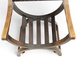 Early 20th century mahogany Savonarola chair, arched leather back with brass studwork, curved open arms with incised geometric decoration, loose patchwork velvet cushion seat, X-frame supports united by circular side rails, on scrolled feet