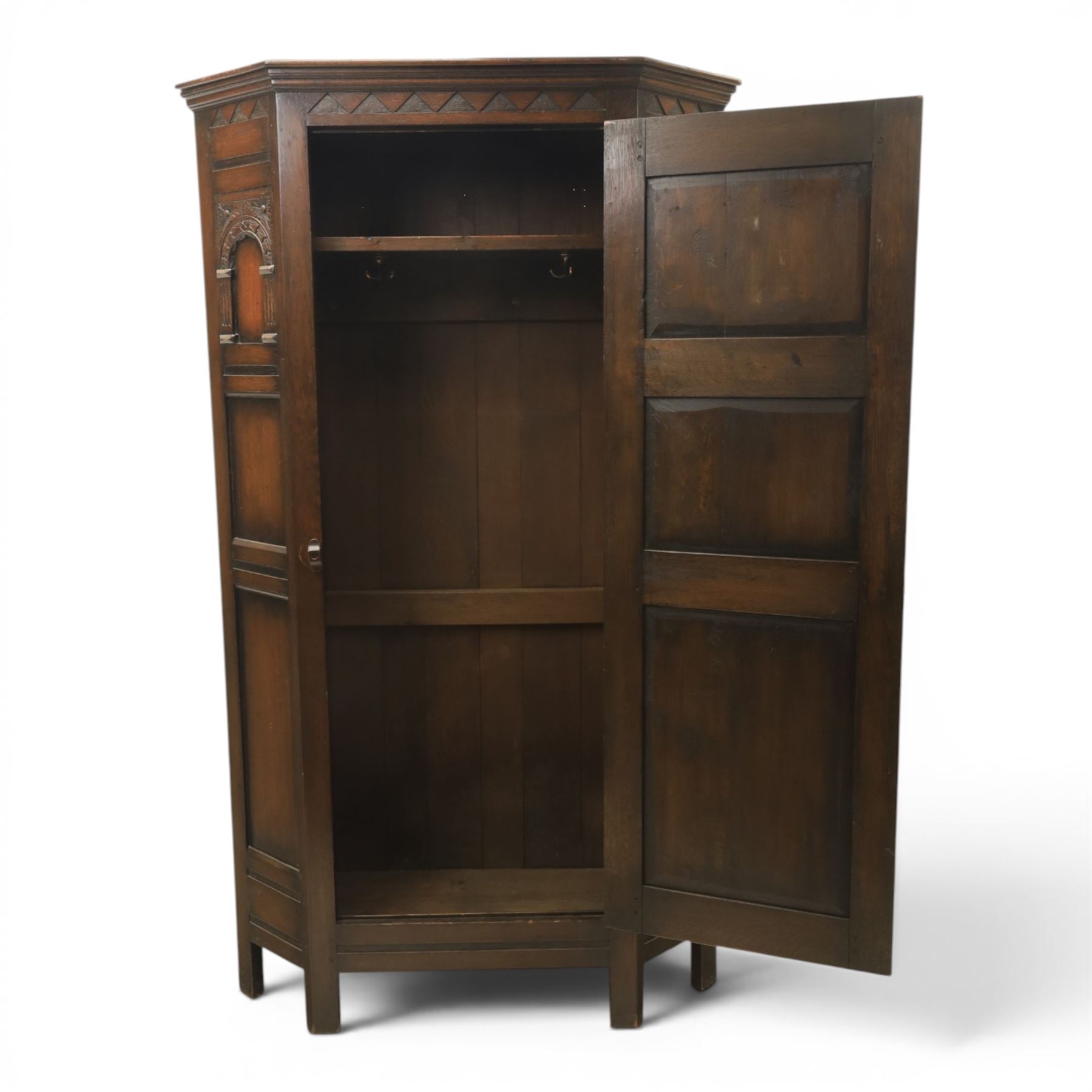 20th century dark stained oak hall robe, cantered sides enclosing a hooks and a shelf, panelled and carved sides, raised on stile supports