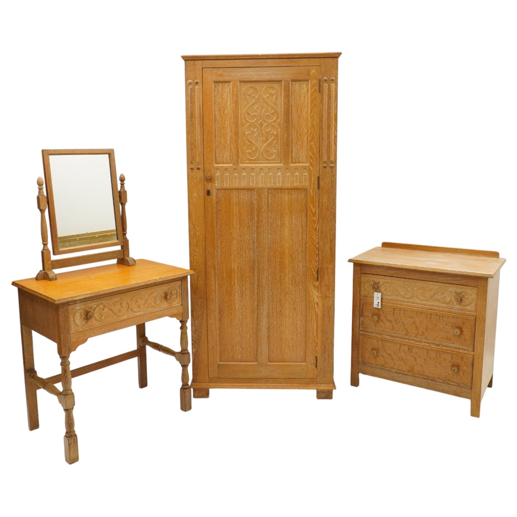 Arts & Crafts design limed oak bedroom suite; comprising dressing table, single wardrobe and chest, with carved scrolling motifs.

Wardrobe (H 181cm, D 47cm, W 79cm)
Chest (H 74cm, D 46cm, W 73cm)
Dressing table (H 136cm, D 47cm, W 74cm)