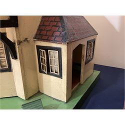 Large Tri-ang No.93 doll`s house in the 'Stockbroker's Range' c1935; two-storey double-fronted Tudor design, half timbered gables, two-storey bay windows, cream and mock shrubbery to front, opening metal framed windows with green shutters, red simulated tiled roof with chimney, integral garage with opening doors, front elevation has four hinged doors opening to reveal two bedrooms with fire places, living room, bathroom and kitchen with built in dresser and sink, entrance hall and staircase, side entrance with porch and seat and sun dial over on chimney stack; some wiring for electrical lighting; metal Tri-ang Toys disc verso; comprehensively furnished H66cm L117cm D43cm