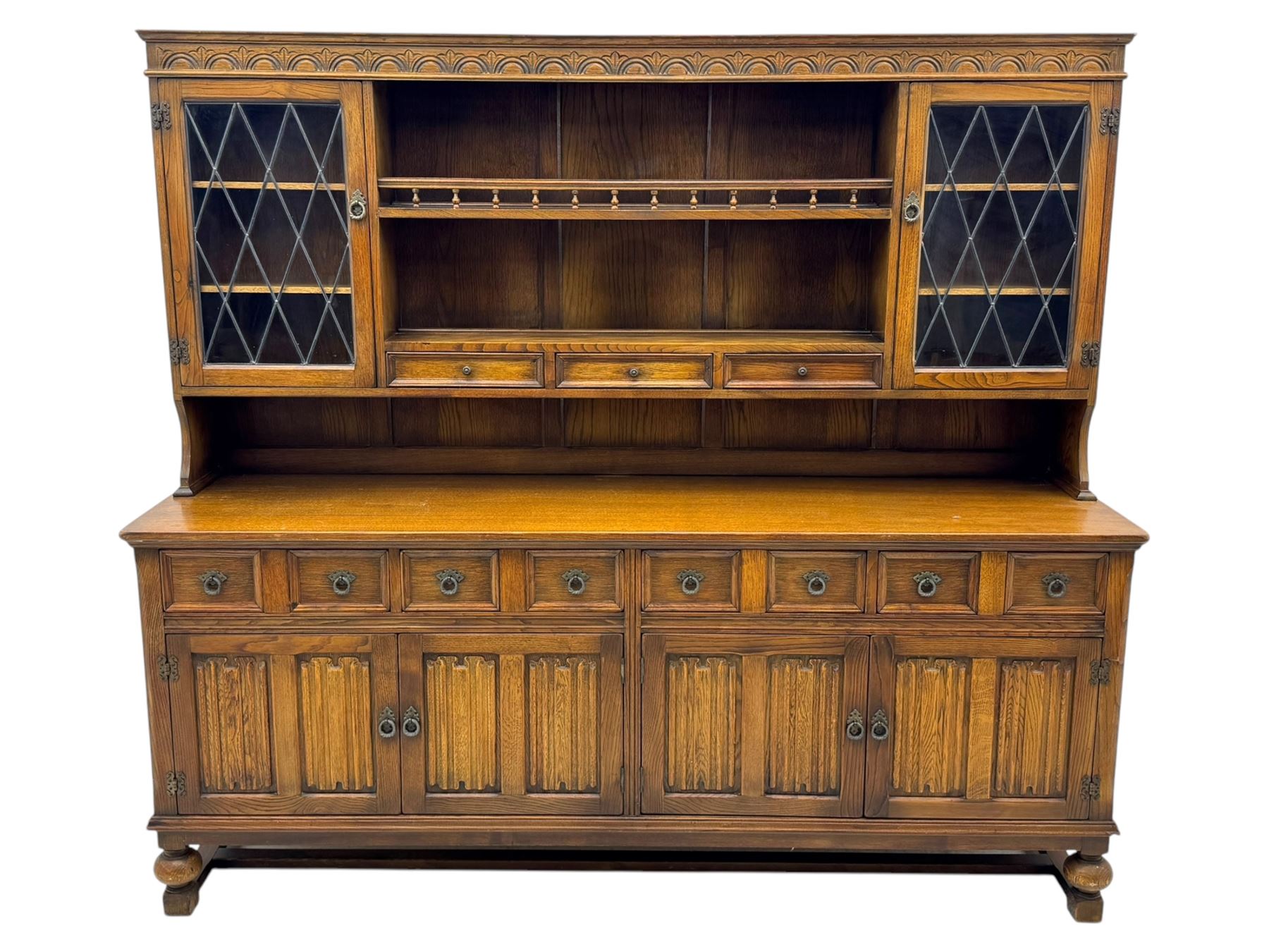 Large mid-20th-century oak dresser with two astragal glazed doors between gallery shelf and lower shelf, with three short drawers and lower section with four drawers and three double-panelled linen-fold hinged cupboard doors 