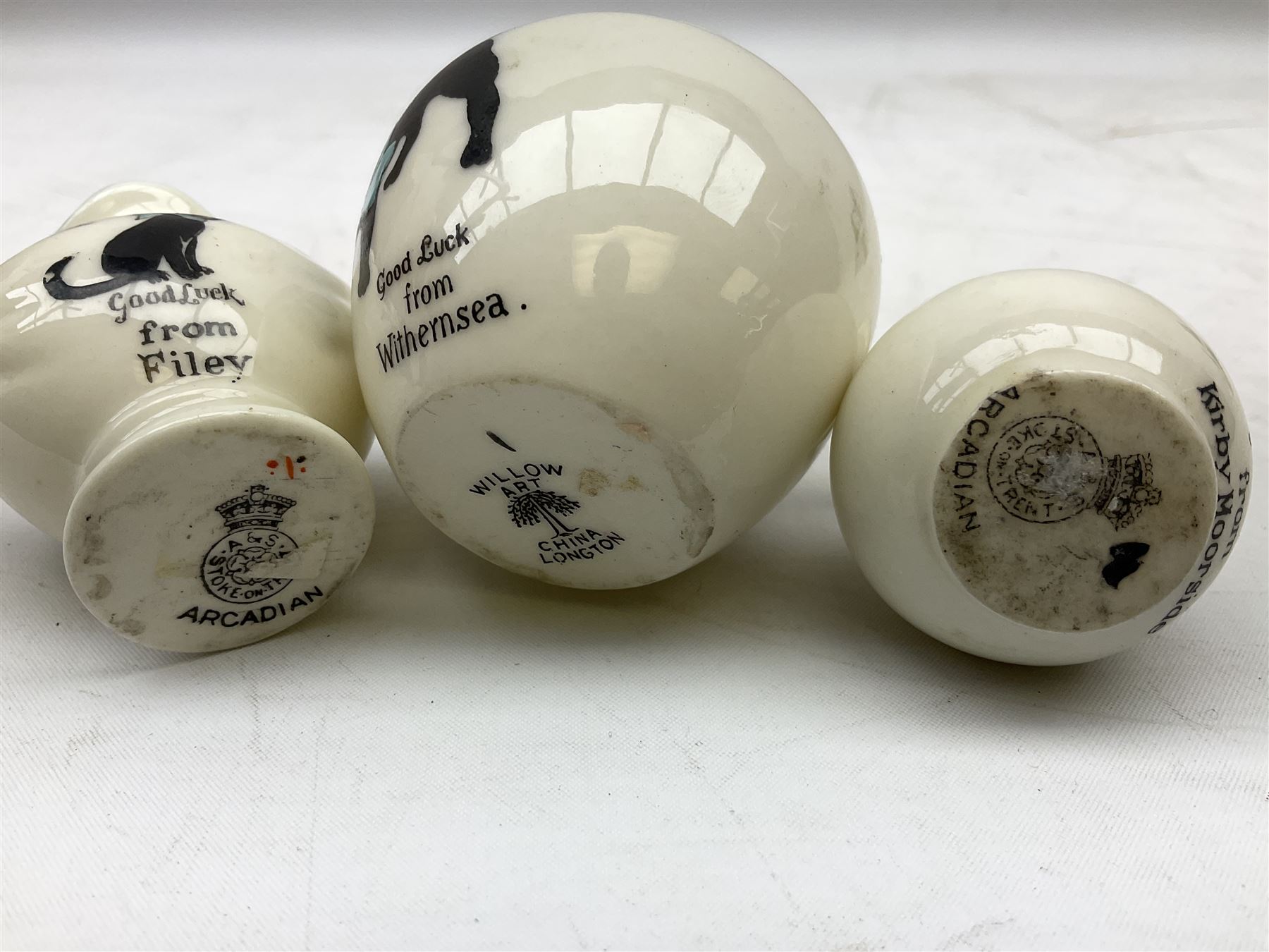 Five crested ware Good Luck black cats, comprising two Willow Art examples, two Arcadian examples and one Carlton China, to include Bridlington, Hull, Filey, etc, tallest H9cm