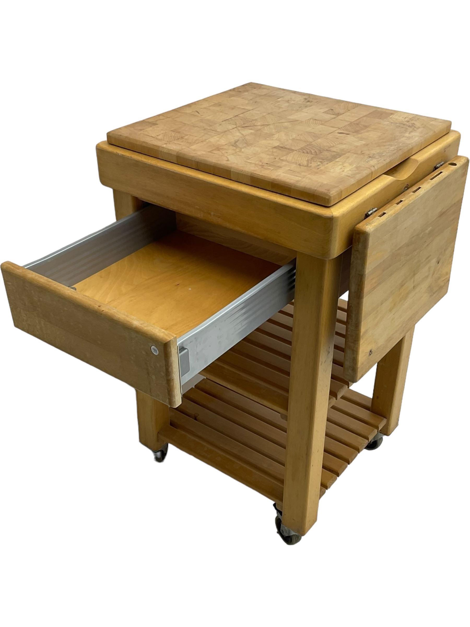 Beech butcher block kitchen cart, featuring square butcher block top, side drop-leaf extension, single drawer with metal sides, and two slatted shelves below, the cart supported by four castors