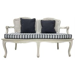 French design white painted two seat serpentine settee, floral carved cresting rail over cane back, loose striped upholstered seat cushion, on cabriole supports