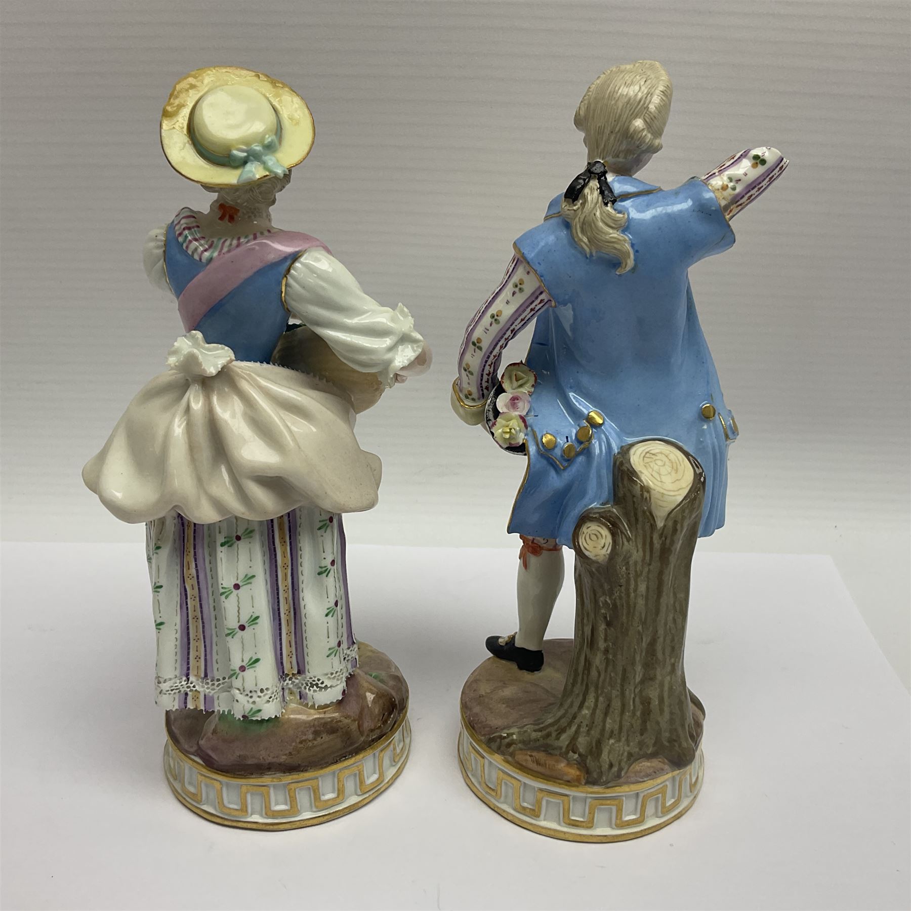 Pair of late 19th/early 20th Century Meissen figures, modelled as flower sellers, after the original by Michel Victor Acier, she holding basket of flowers, he holding flowers in his hat, each with underglaze cross swords mark beneath, tallest H16.5cm
