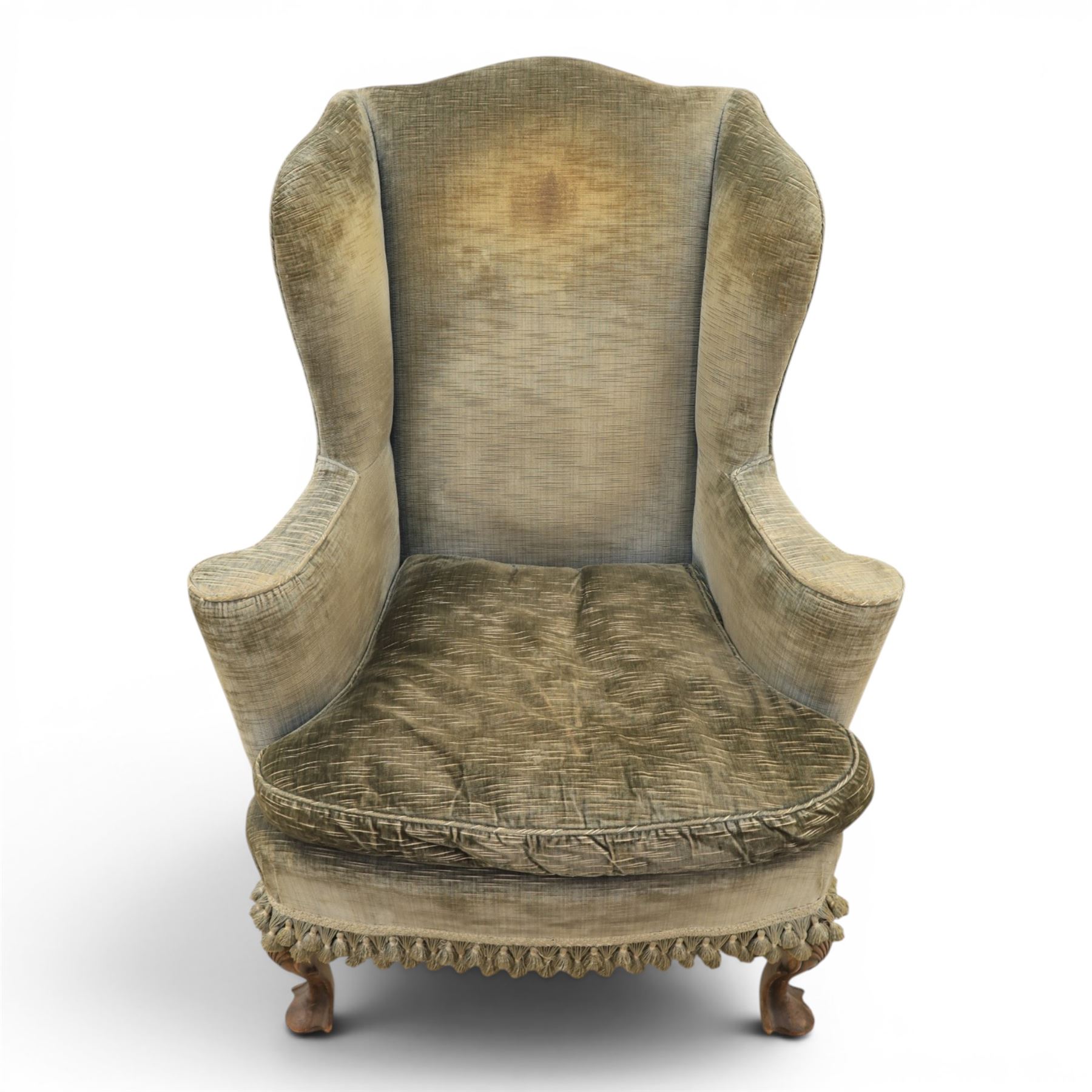 Pair of Georgian style wing armchairs, upholstered in green velvet, each with shaped wing backs, padded scroll arms and loose seat cushions, raised on cabriole supports terminating in pad feet, one with tasselled fringe