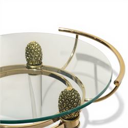 Hollywood Regency style gilt metal and glass serving trolley, circular top in a polished brass surround with three pineapple finials, supported on clear column legs, lower glass shelf enclosed by a brass gallery, terminating in castors