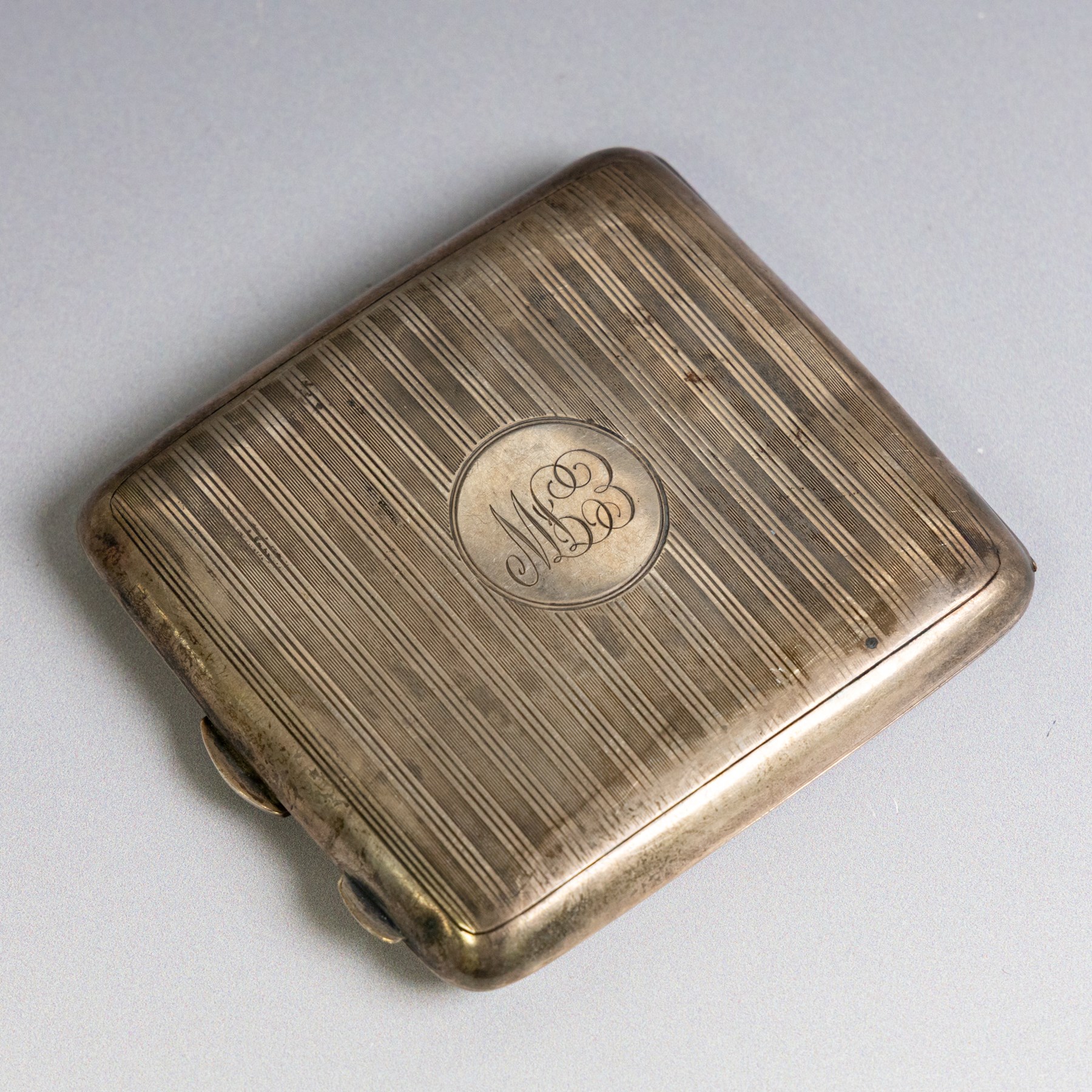Two early 20th century silver cigarette cases, comprising a rectangular example with foliate decoration and vacant shield cartouche and a 1920s example with engine turned decoration and engraved initials, both hallmarked
