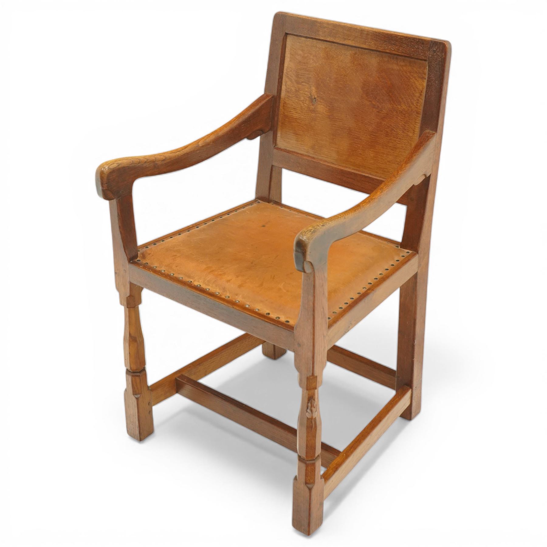 Mouseman - oak panel back carver armchair, lightly adzed panel back above a tan seat with brass studded trim, flanked by swept arms raised on octagonal front supports, with carved mouse signature, by the workshop of Robert Thompson of Kilburn