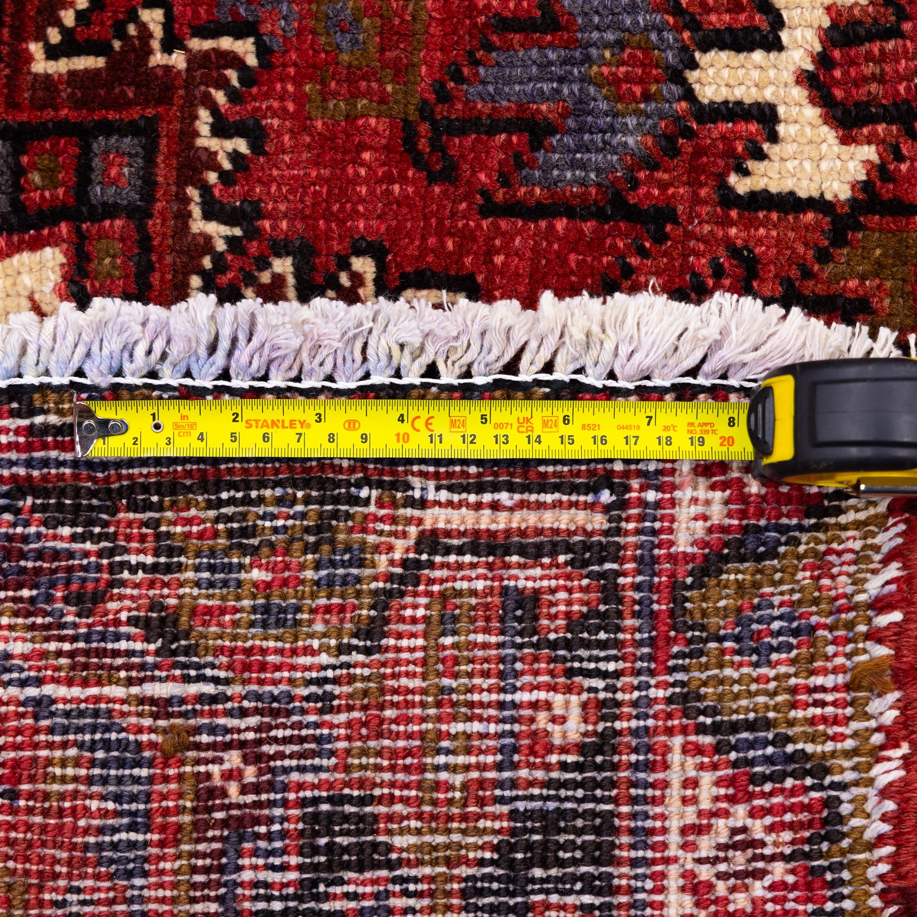 North West Persian Heriz hand-knotted carpet, madder red field, with a large central angular star medallion with stepped outlines on ivory ground, surrounded by geometric floral devices and stylized rosettes, with corresponding corner spandrels, enclosed by a bold geometric main border with multiple guard stripes, with cotton fringe ends 