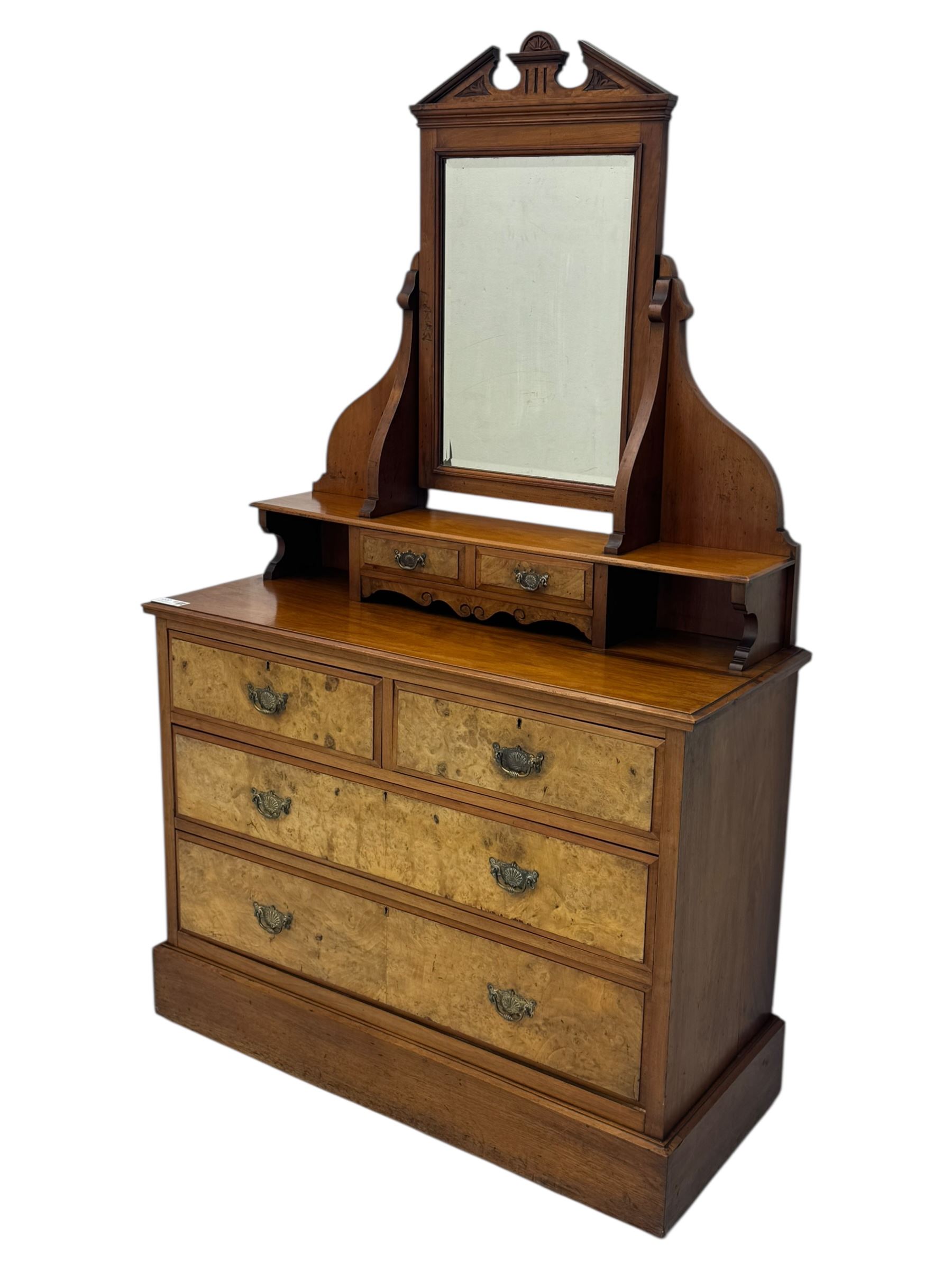 Victorian walnut bedroom suite - wardrobe, dressing chest and bedside cupboard, comprising a full-length wardrobe with broken pediment and central mirrored door, large lower drawer, a matching dressing table with bevelled swing mirror over two trinket drawers and two short drawers over two long drawers, and a single-door bedside cupboard, all with moulded edges, decorative panel work and shaped aprons