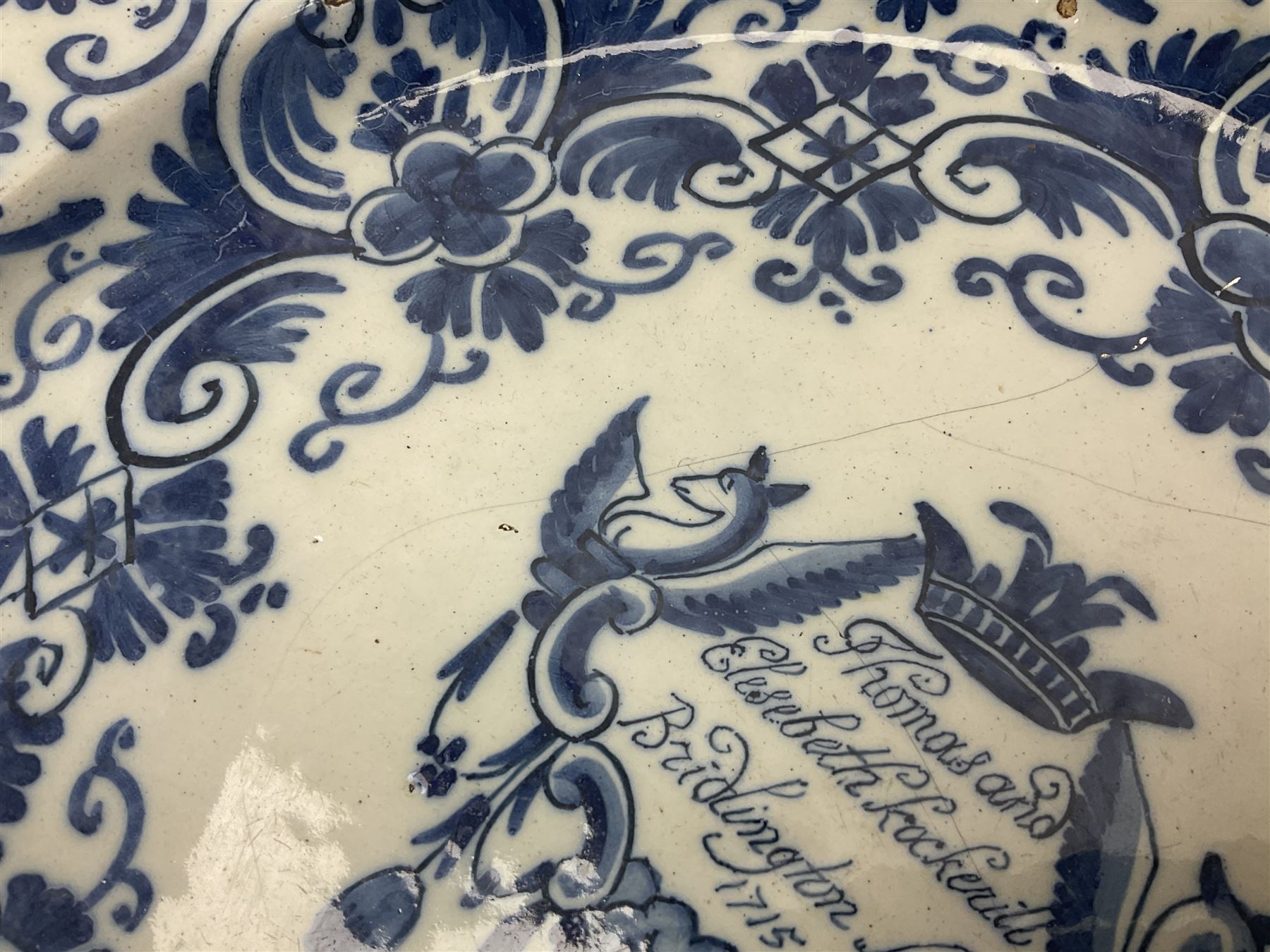 Early 18th century Delft marriage plate, of circular form with dished centre, the centre inscribed and dated 'Thomas and Elizabeth Kockerill Bridlington Key 1715' within a crowned C scroll cartouche, flanked by demi-griffins, above a putto head and tassels, within a wide foliate border, D34cm
