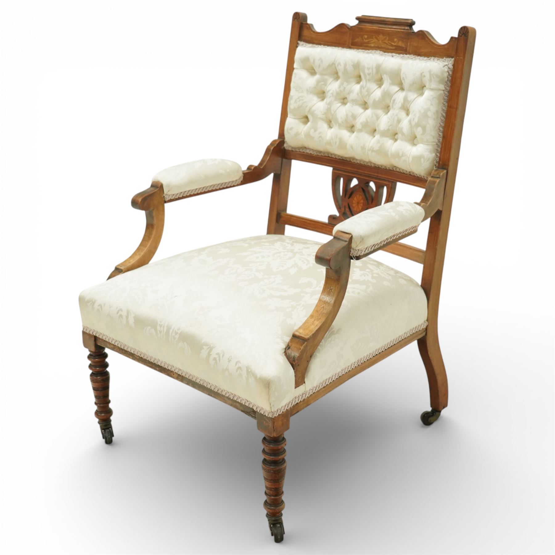 Edwardian mahogany open armchair, the upholstered rectangular back buttoned in ivory patterned fabric within a shaped top rail with inlaid foliate detail, open splat carved with a pierced anthemion motif centred by an inlaid roundel, swept open arms with upholstered pads, over a sprung upholstered seat, on turned front supports with brass castors