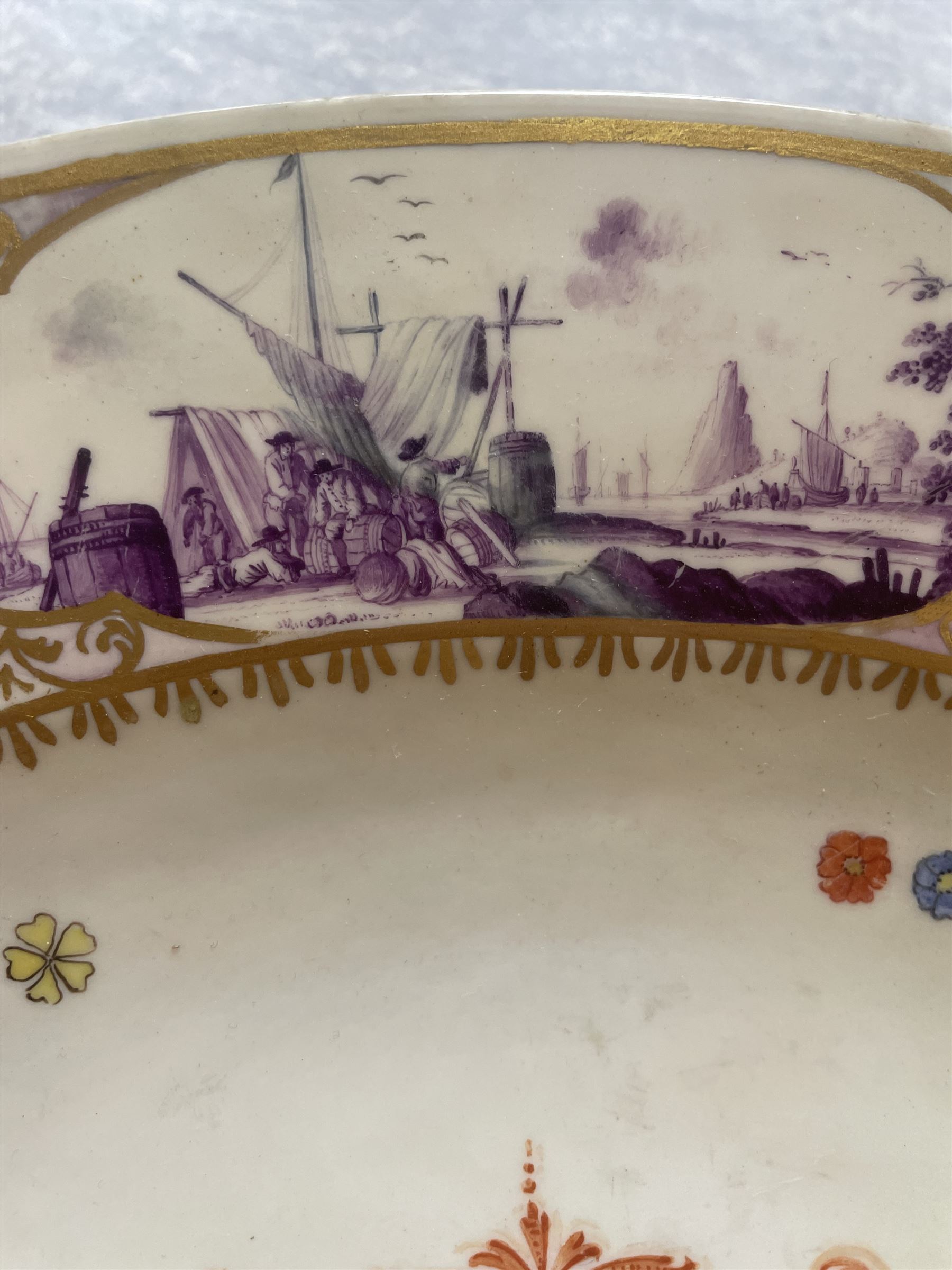 Large and impressive 18th century Meissen dish, finely painted with a chinoiserie scene to a central shaped reserve, depicting figures and attendants engaged in various pursuits, the reserve with gilt scrollwork edge, filled with Böttger lustre and detailed with iron red scrollwork, surrounded by flower heads, the rim with four quatrofoil Kauffahrtei scene panels of merchants and figures by a quayside in purple monochrome, with gilt scroll border, with under glazed blue crossed swords mark, and gilt gilders mark, D39cm

