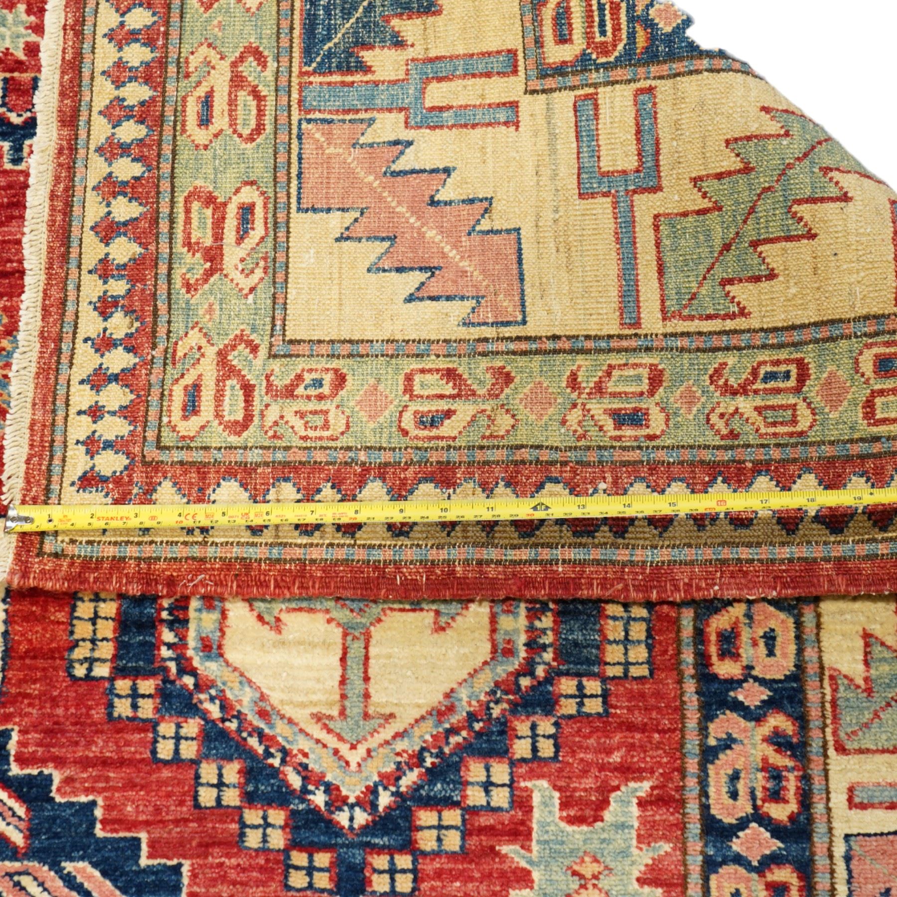 Caucasian Kazak hand-knotted rug, madder red field with bold geometric medallions and angular tribal motifs, within multiple patterned borders in a palette of indigo, red, ivory and green 