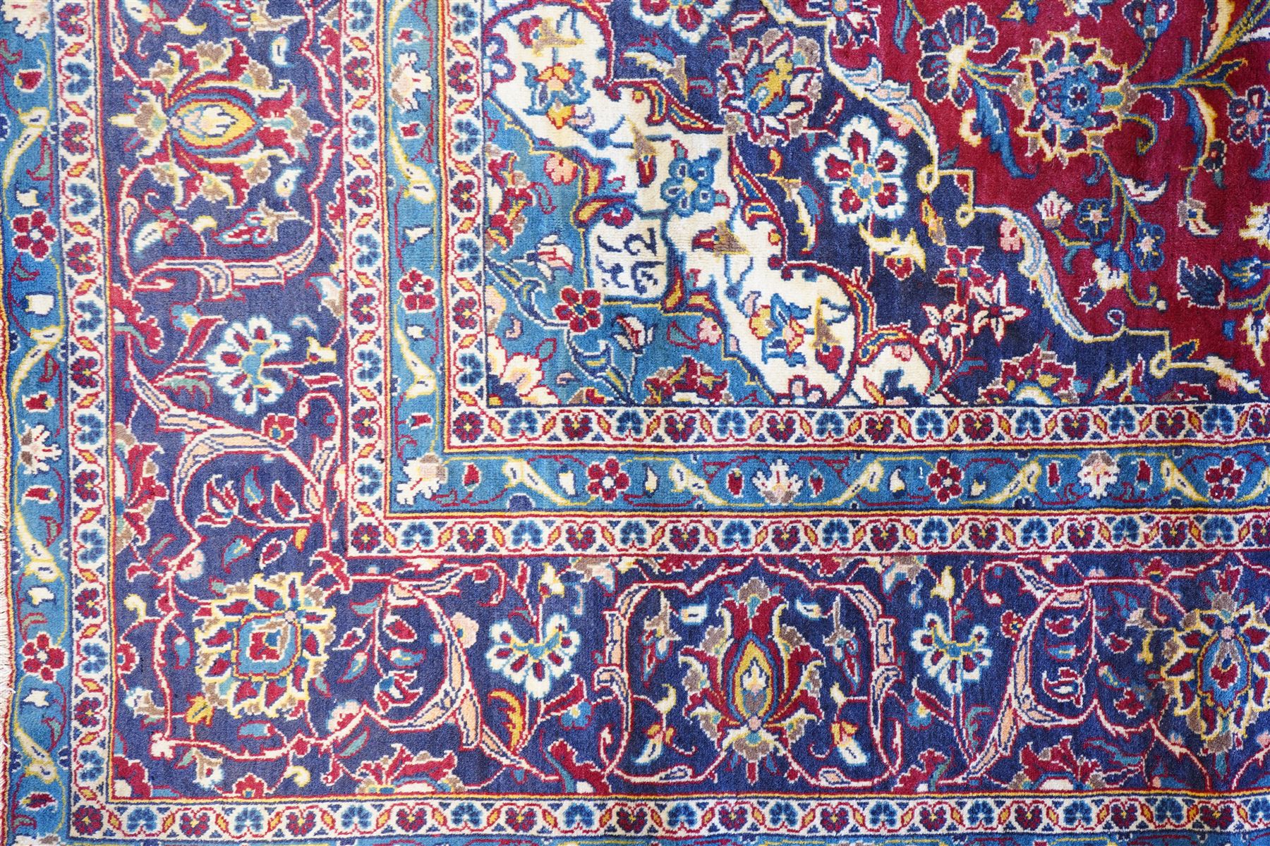 Central Persian Kashan hand-knotted carpet, crimson field with a central elaborate cusped medallion surrounded by elegant scrolling floral vine design incorporating stylized palmettes, rosettes and foliate sprays and similarly decorated spandrels enclosed by a dark indigo main border of floral arabesques between multiple guard stripes, cotton fringe ends 