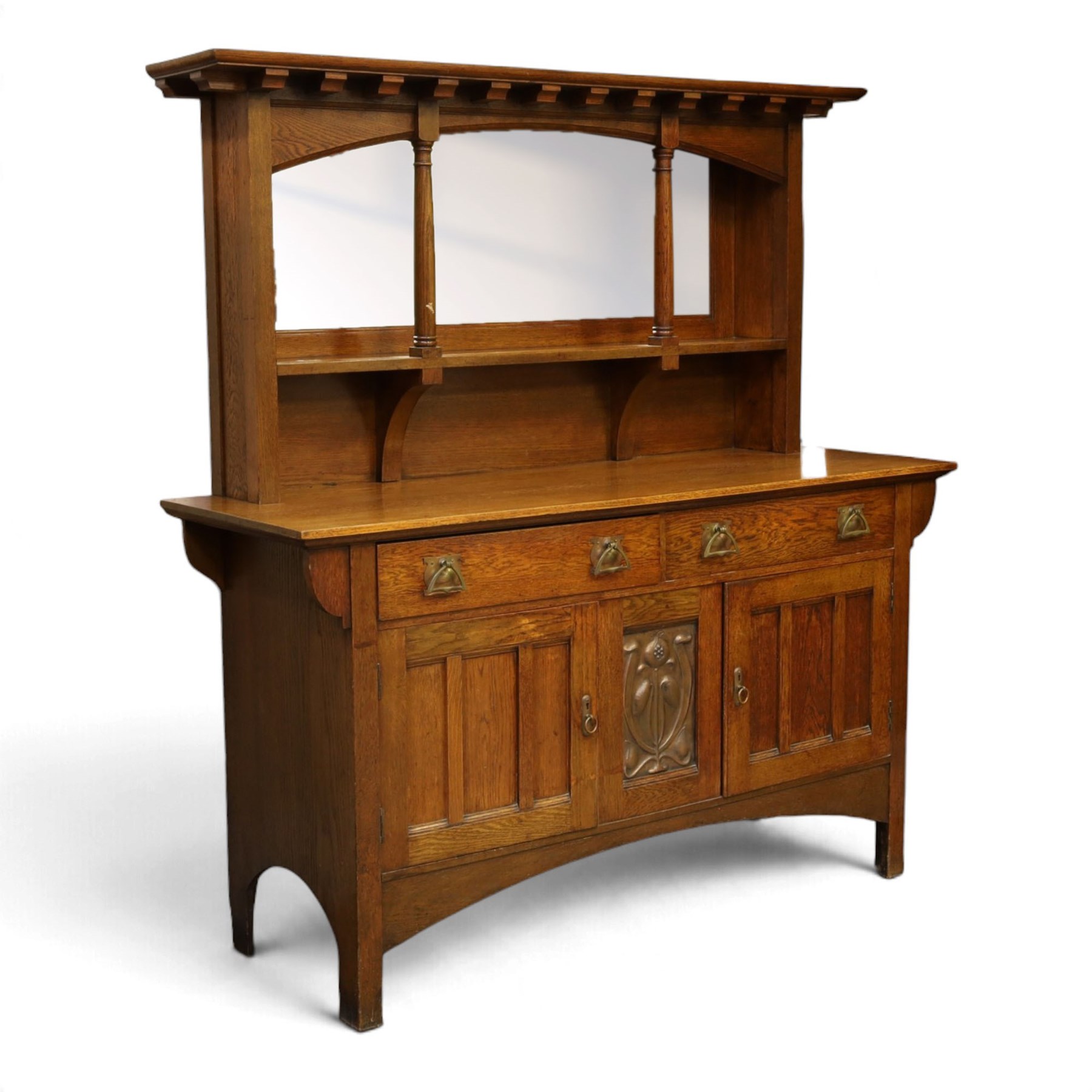 Art Nouveau oak mirrored sideboard, in the manner of Liberty's London, the raised back fitted with bevelled mirror plates divided by turned supports beneath a projecting cornice, above two drawers and panelled cupboard doors, the central panel applied with stylised floral carved panel, raised on shaped feet