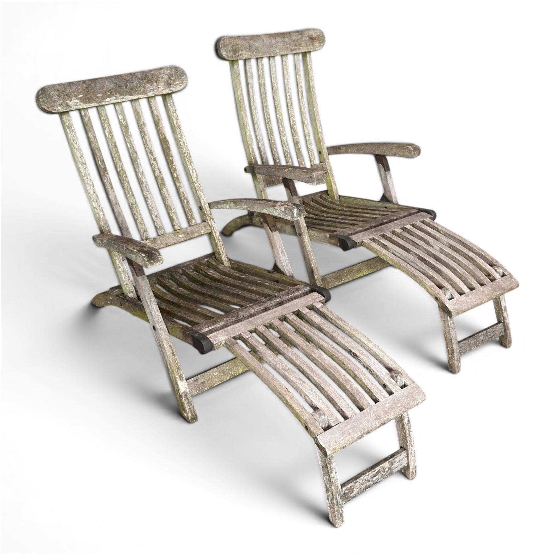 Pair of teak reclining garden steamer armchairs, each with an adjustable slatted back, curved slatted seat and footstool