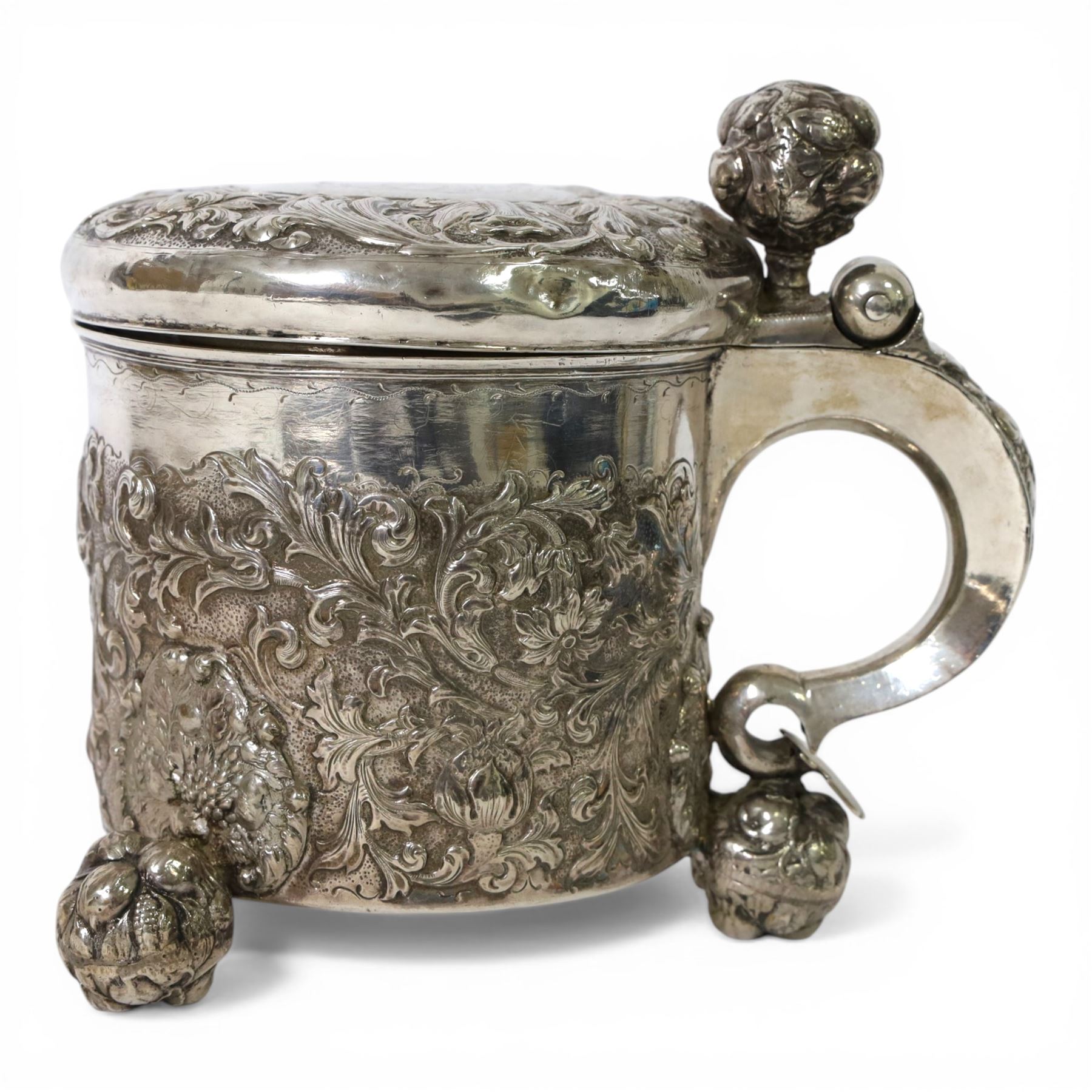 Northern European silver peg tankard, probably late 18th/early 19th century, of cylindrical form, the body repoussé decorated with scrolling and blossoming acanthus, fitted with scroll handle with shield terminal, the hinged cover with conforming repoussé decoration surrounding a central circular panel engraved with monogram beneath initials EASBGD, opening with ball thumbpiece detailed with fruits, raised upon three confirming ball feet mounted with shaped panels also detailed with fruits, bearing indistinct mark beneath, H19cm