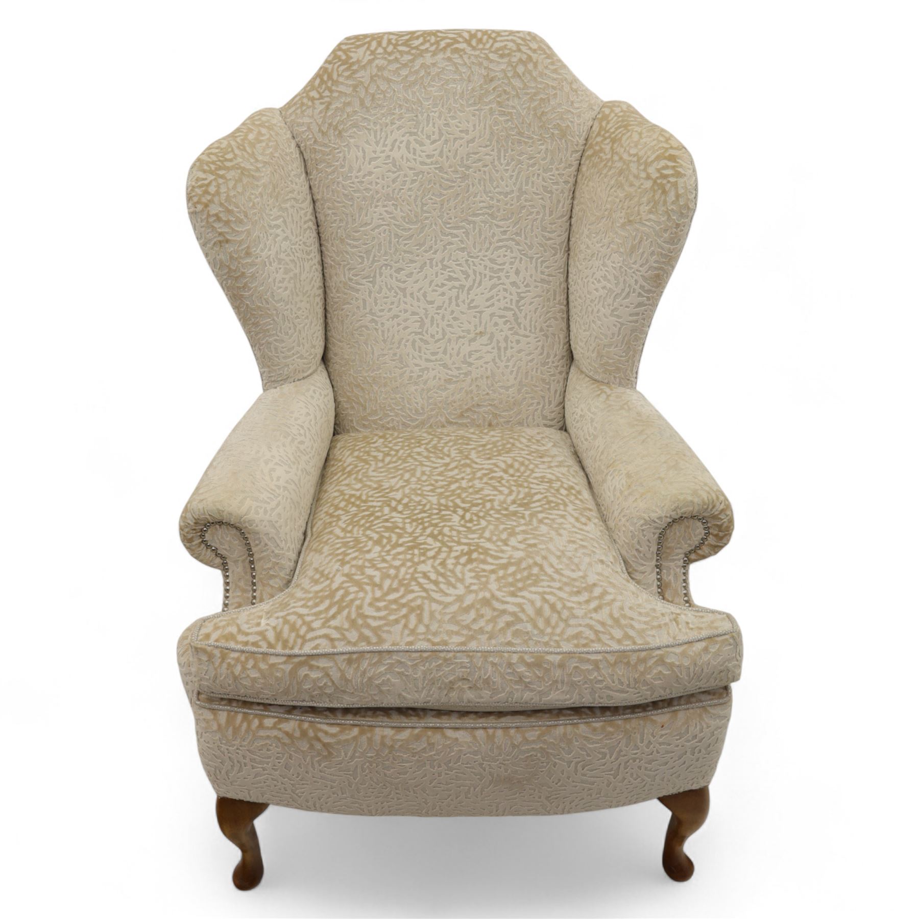 Late 20th century wingback armchair and matching footstool, upholstered in beige embossed fabric with brass stud edging, on cabriole legs and splayed rear legs, together with a matching footstool on turned supports terminating in brass castors (Stool H 42cm, W 75cm, D 47cm)