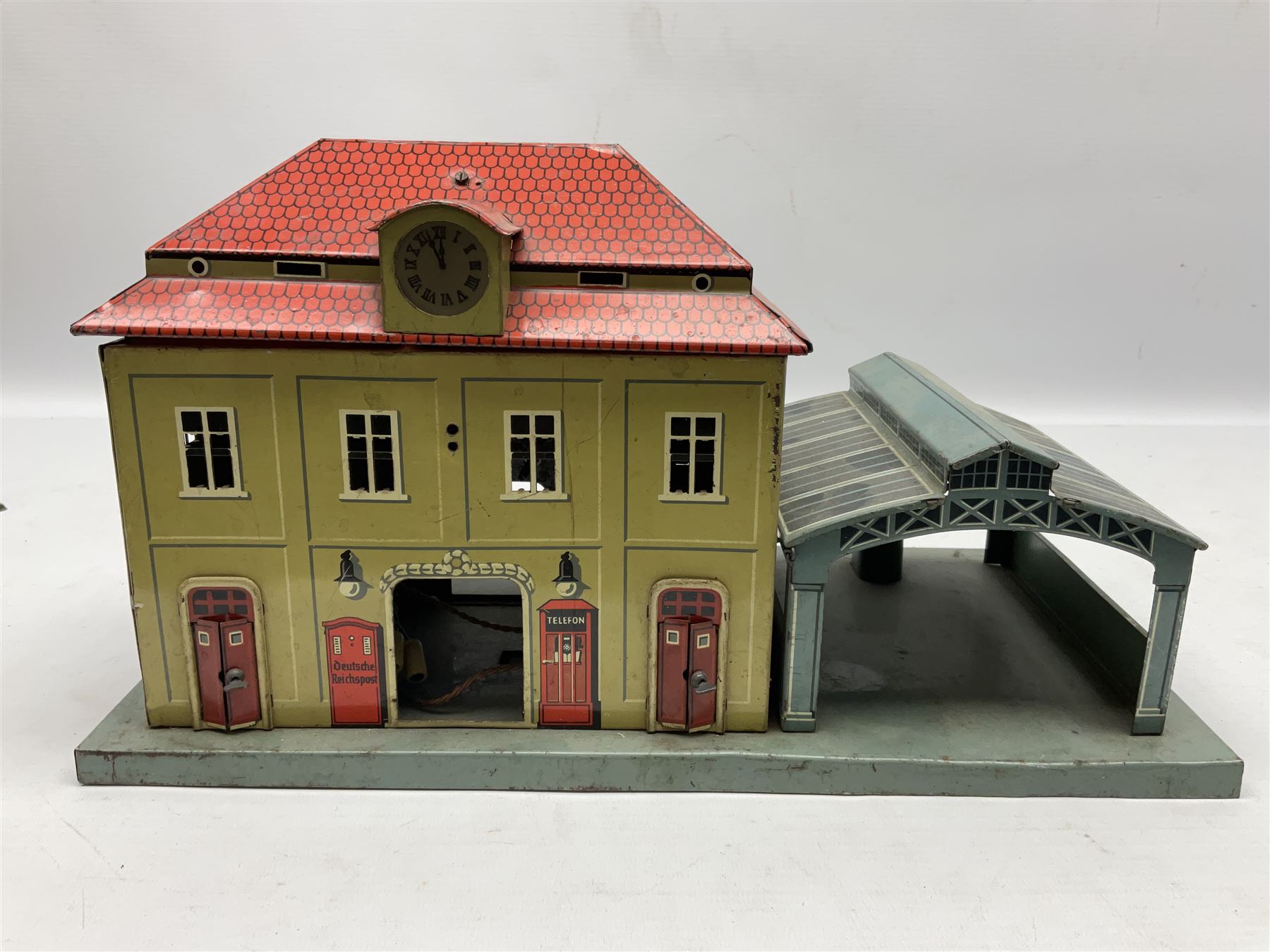 '0' gauge - Bing tin-plate two-storey double sided station with open walk-through to one end, rail side canopy, hinged doors and removable roof giving access to clock illumination L35cm; Bing hand-cranked turntable and open wagon; Marklin tin-plate level crossing barrier and Newspaper vendor's tin-plate four-wheel hand cart (5)
