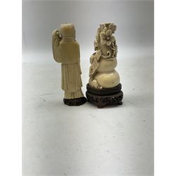 Two carved ivory figures, comprising of man standing holding a vine leaf and the other seated at the base of a tree, both on carved wooden platforms, tallest example H11cm