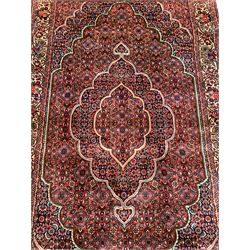 Persian Bidjar crimson ground rug, thick woollen pile, the field decorated with repeating Herati motifs within cusped outlines, the guarded border decorated with repeating flower head motifs