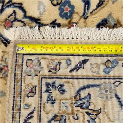 Central Persian Kashan hand-knotted carpet, ivory ground, with a central pale blue shaped floral medallion with pendants, surrounded by scrolling foliate and floral motifs incorporating rosettes, palmettes and delicate vine work in blue, cream and beige tones, enclosed by an ivory border with repeating palmettes and meandering vines, flanked by floral guard stripes, with cotton fringes