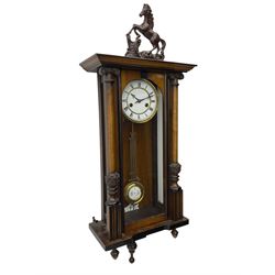 A late 19th century German spring driven 'Vienna' wall clock with a fully glazed door flanked by turned columns with ionic capitals and carving, replacement pediment depicting a prancing horse, with a two-piece enamel dial, Roman numerals, minute track and gothic steel hands, 8-day movement striking the hours and half hours on a gong,  with a gridiron pendulum and beat plate. With key.


