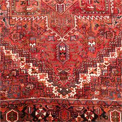 North West Persian Heriz hand-knotted carpet, madder red field, with a large central angular star medallion with stepped outlines on ivory ground, surrounded by geometric floral devices and stylized rosettes, with corresponding corner spandrels, enclosed by a bold geometric main border with multiple guard stripes, with cotton fringe ends 