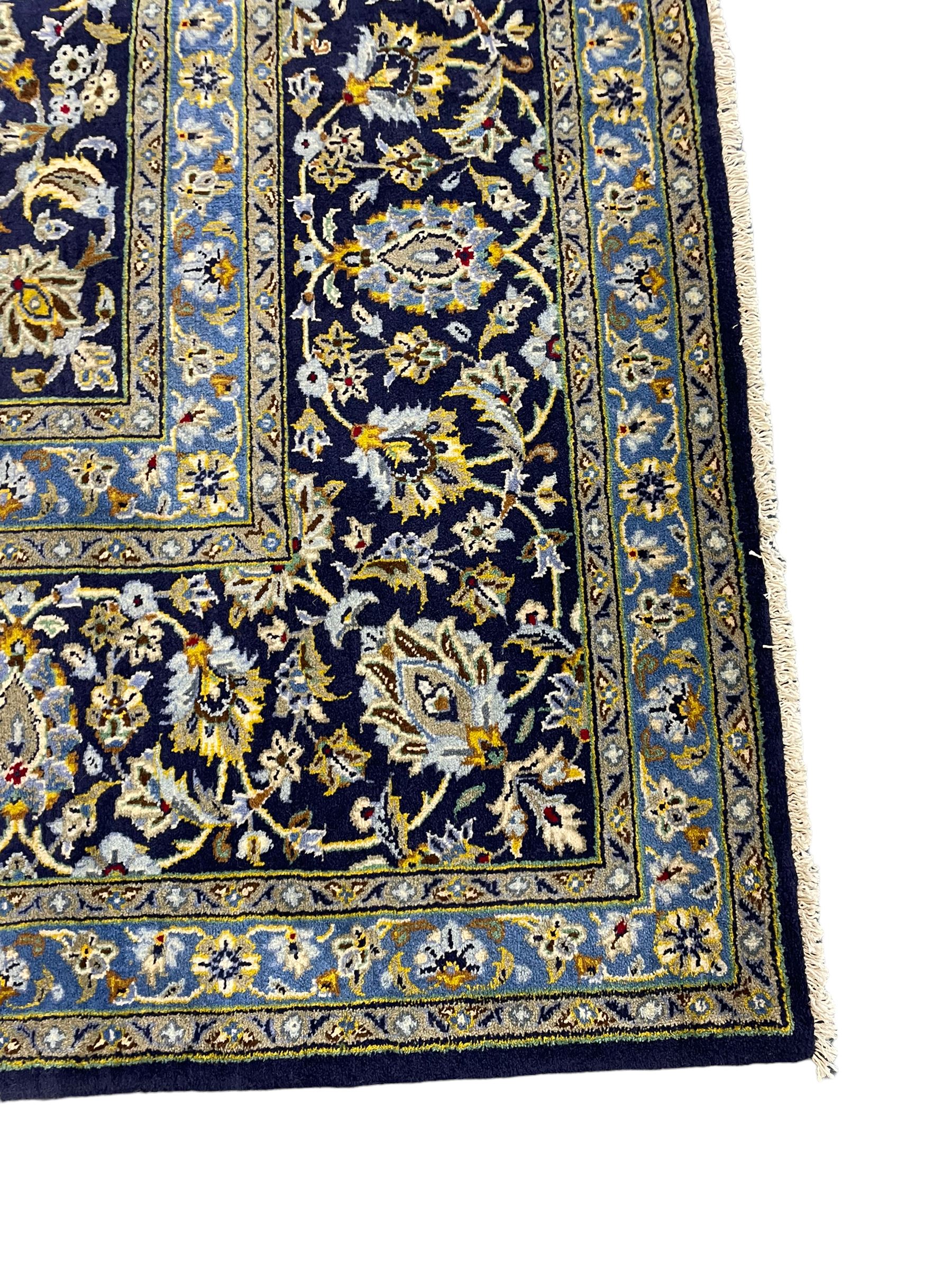 Central Persian Kashan indigo ground carpet, central lighter blue floral medallion surrounded by interlacing leafy branches and stylised plant motifs, the main border decorated with repeating floral motifs and scrolling branches, within guard stripes 