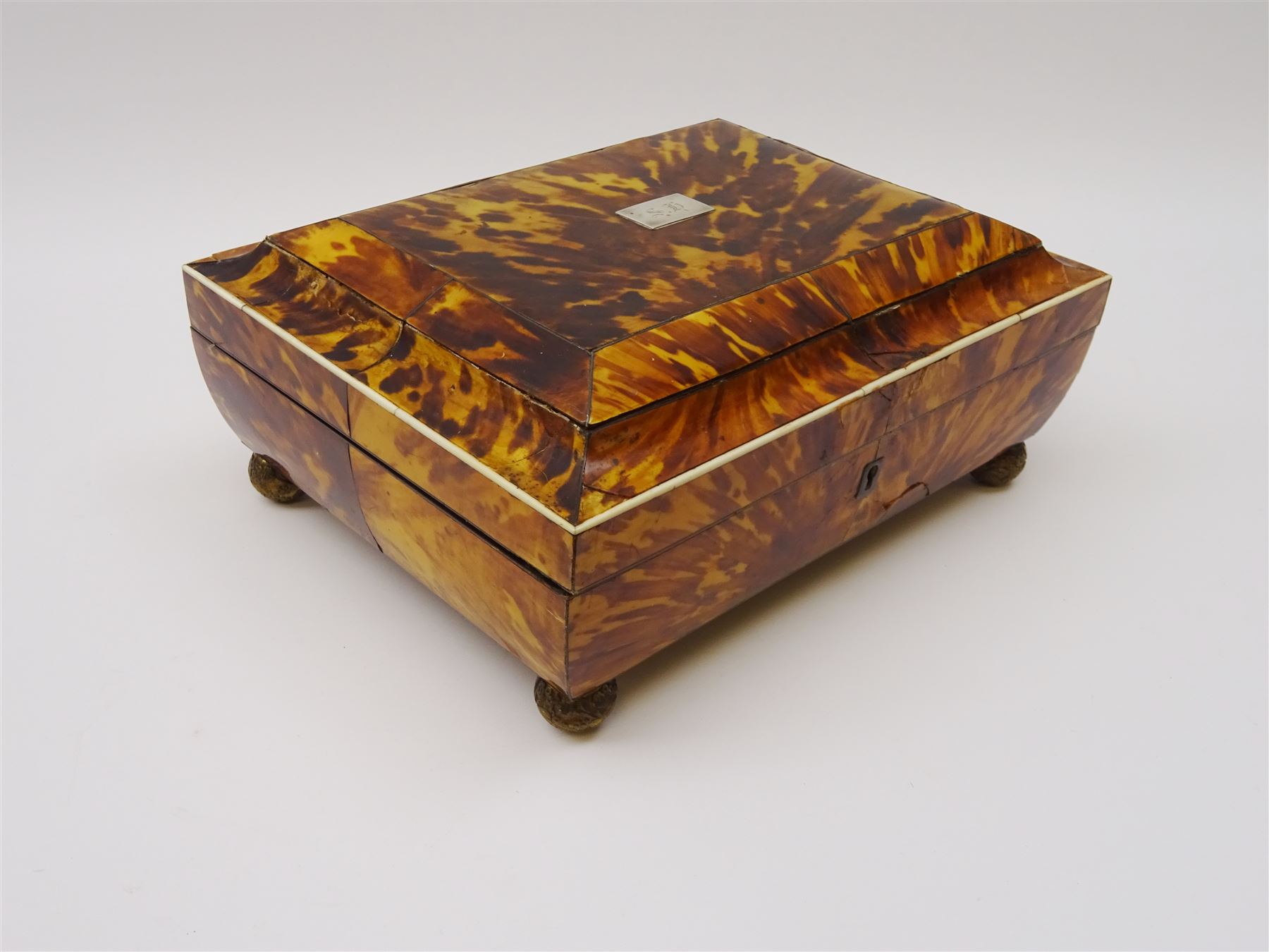 19th century tortoiseshell sewing box, of sarcophagal form upon four foliate detailed brass ball feet, the hinged cover edged in ivory with initialled silver plaque to centre, opening to reveal a silk lined interior, H9.5cm W22.5cm D18cm