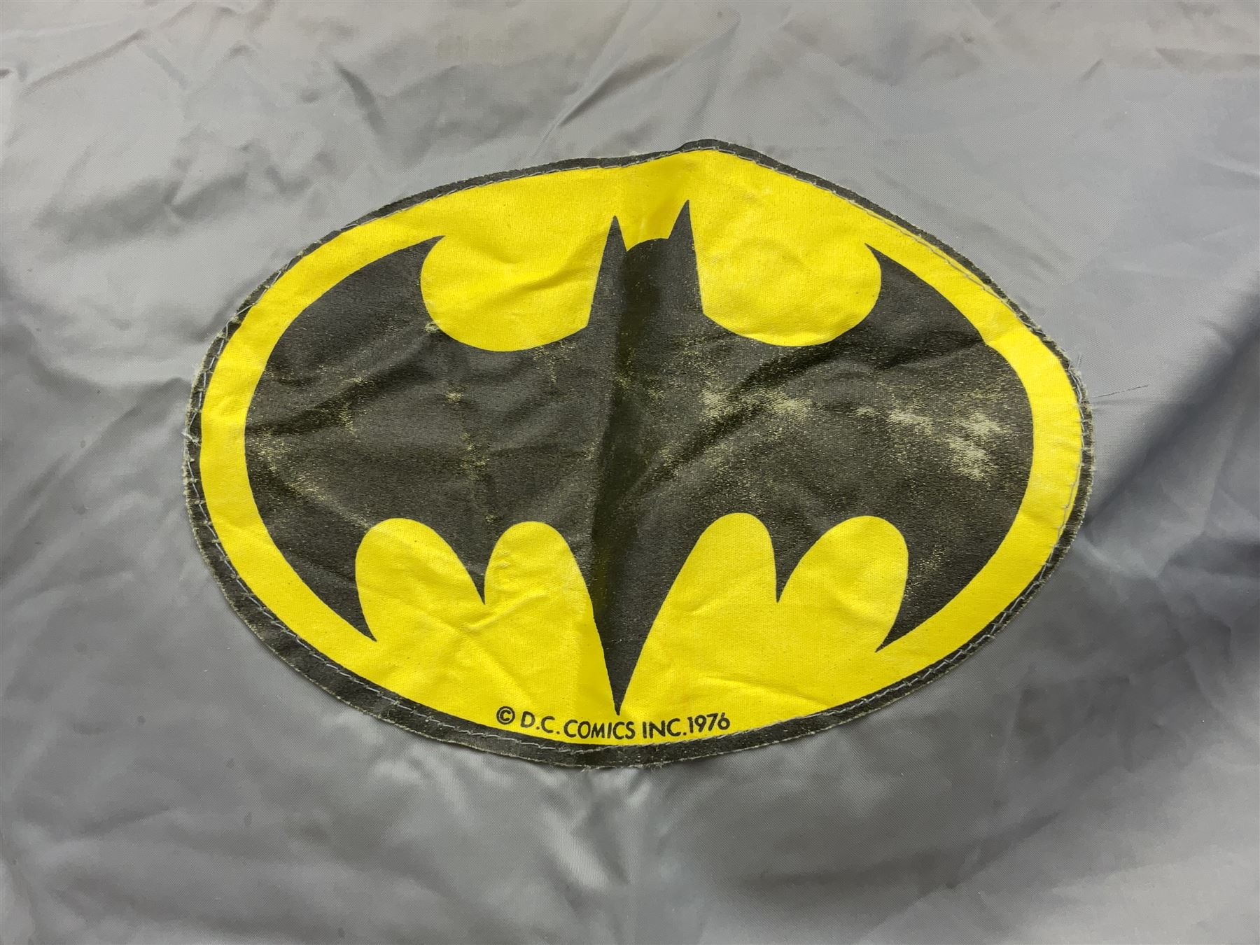 Two Boxed Batman Playsuit Costumes - 1960s 20th Century Original Play Suit, black eye mask, plastic vinyl cape/gauntlets, leather style belt, blue/yellow shirt, with Bat motif and blue/yellow pants; in original illustrated lidded box; and 1976 Decker Batman Playsuit costume, vinyl cape/ mask/gloves/boot tops/yellow belt, grey cloth top and pants; in original illustrated box (2)