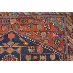Persian Heriz hand-knotted carpet, terracotta ground centred by large dark navy geometric medallion with stepped outline, decorated throughout with stylised flowerheads, palmettes and geometric motifs in blue, green and ochre, enclosed by diagonal geometric border with narrow guard stripes