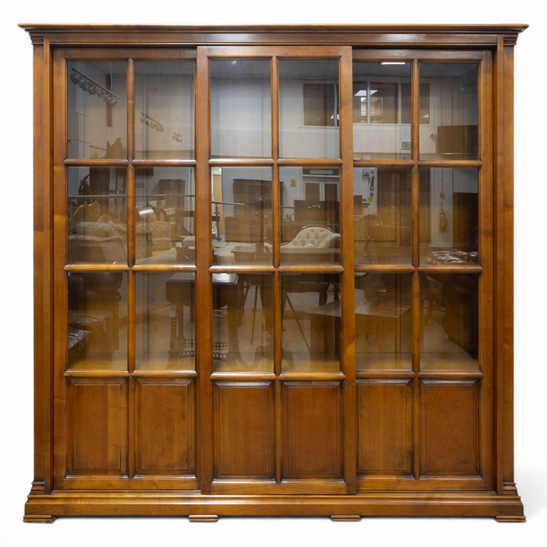Wesley Barrel - large cherry wood bookcase, with projecting cornice and fielded panelled sides, with three sections comprising three fixed shelves, sliding glazed and panelled doors, moulded plinth base