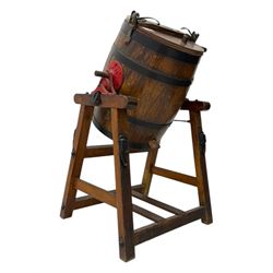 19th century oak and cast iron rotary butter churn, with coopered barrel body, domed lid with filler opening and cast iron securing arms, on tilting iron-mounted frame with crank handle and support rails
