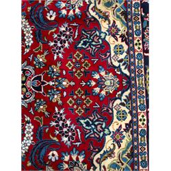 Central Persian Isfahan Carpet, hand-knotted, featuring a bold central rosette medallion on a rich red field, flanked by stylised floral sprays, scrolling foliage and mythical animals, within a broad indigo border decorated with alternating cartouches and flowerheads