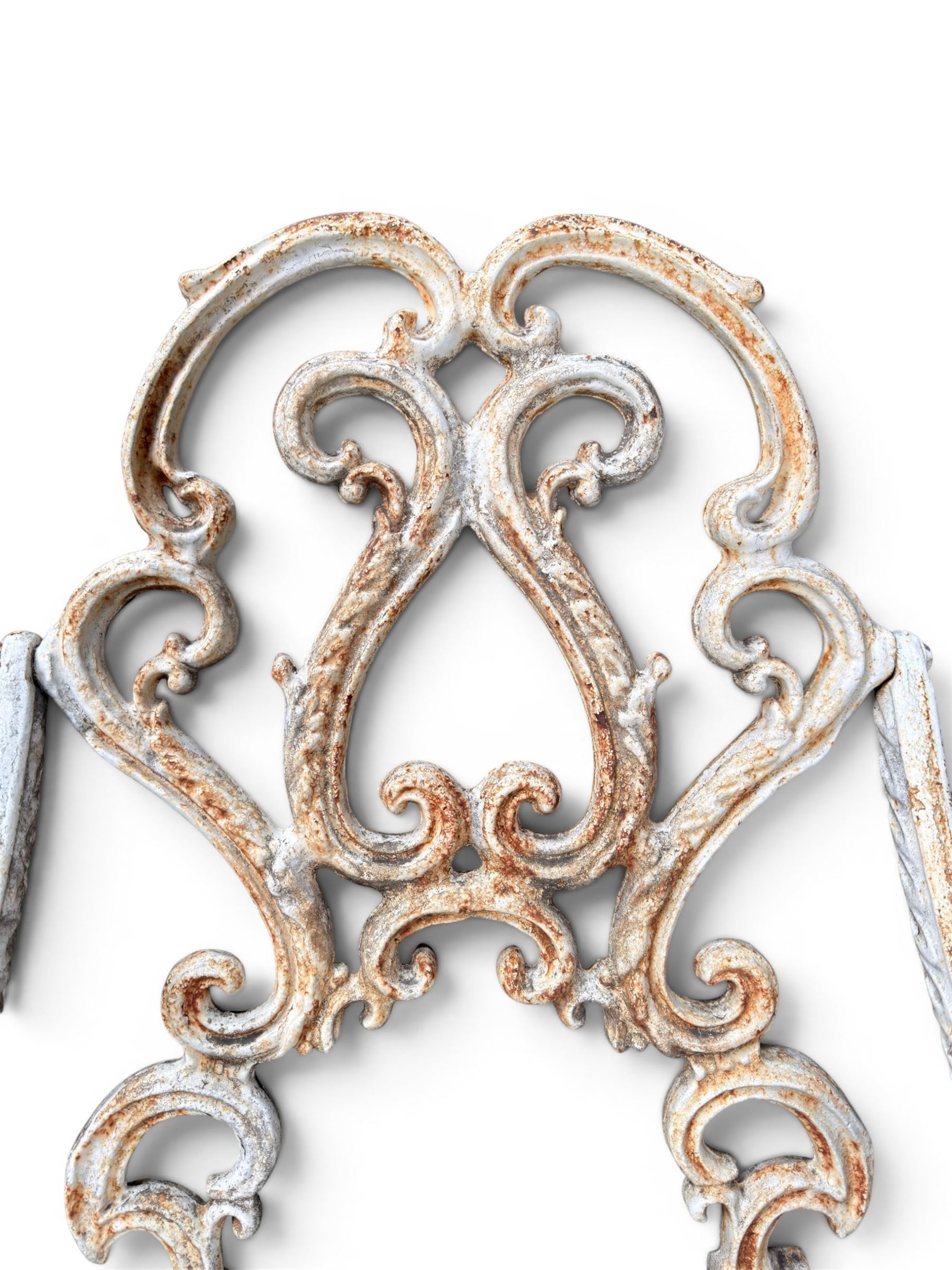 Pair of Victorian cast iron garden chairs, the ornate pierced back of scrolling foliate design, scrolling arm terminals over splayed supports formed of C and S-scrolls, in distressed white painted finish