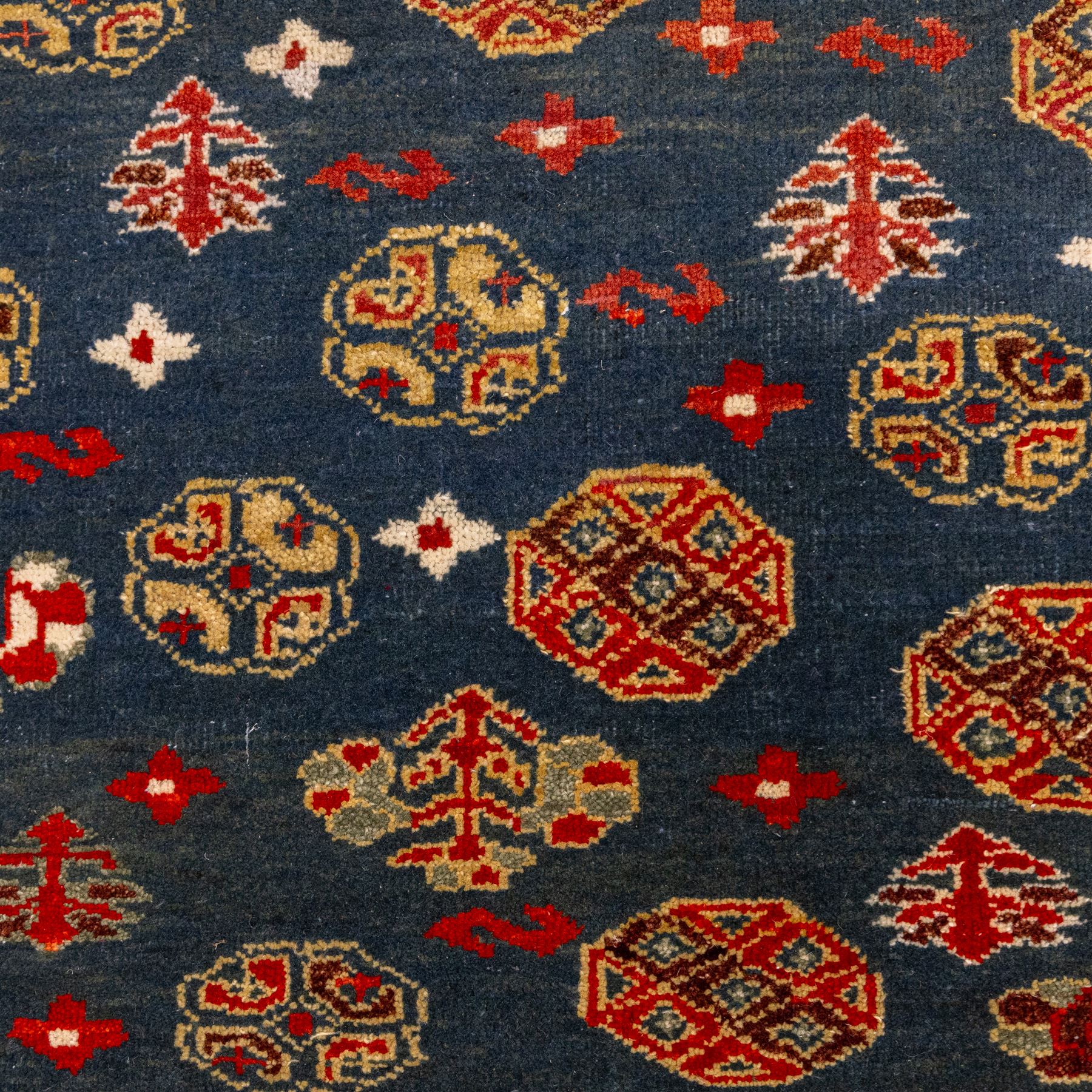 North East Persian Turkoman hand-knotted rug, deep teal blue field decorated with repeating rows of stylized octagonal guls and cruciform tribal motifs arranged in a lattice formation, enclosed composition featuring angular devices and reciprocal motifs, with cotton fringe ends