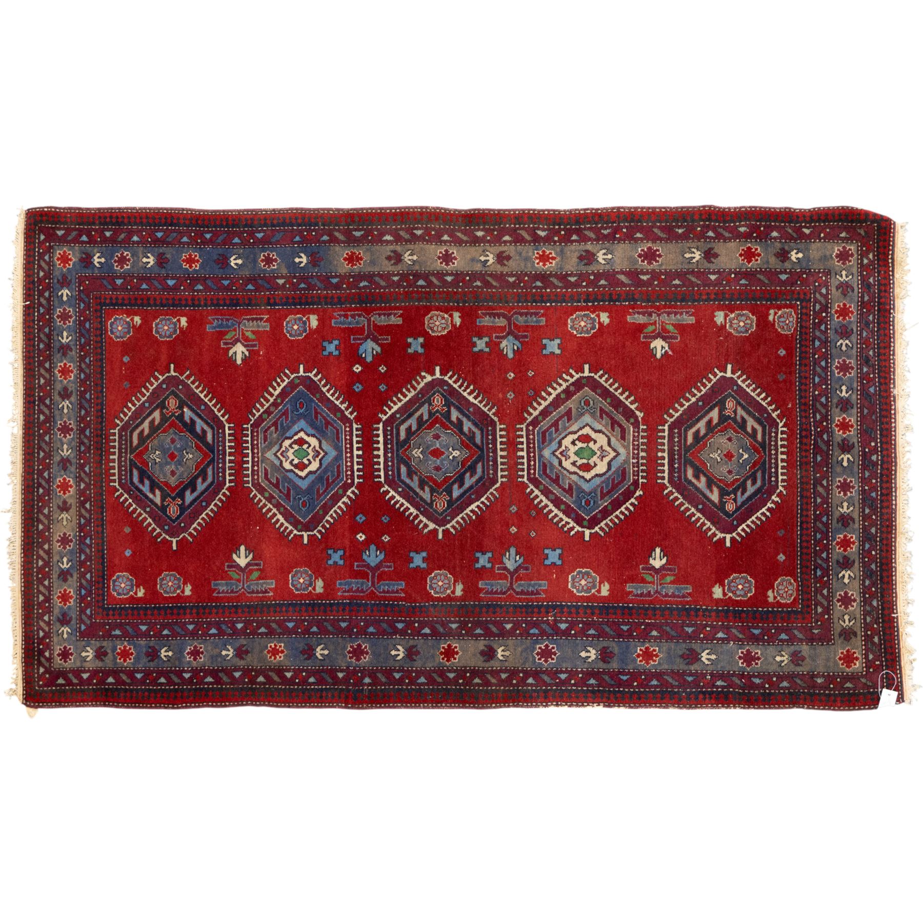 Caucasian Kazak rug, red field decorated with a column of stepped hexagonal medallions in blue, ivory, and crimson, flanked by stylized floral and geometric motifs, enclosed by multiple borders of rosettes and hooked designs 