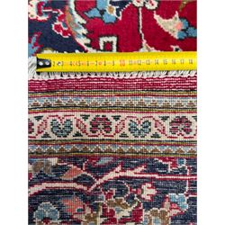 Central Persian Kashan hand-knotted carpet, the deep red ground with a central lozenge medallion in ivory and navy, surrounded by dense scrolling floral and vine motifs, navy spandrels and a wide border with stylised palmettes and flowerheads enclosed by multiple guard stripes