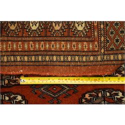 Bokhara hand-knotted carpet, terracotta ground with repeating rows of Tekke guls interspersed with geometric motifs, enclosed by multiple stylised floral and geometric borders, with fringed ends