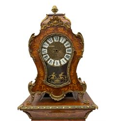 A contemporary 20th century Boulle clock case on a conforming tapered plinth with a glazed door supported on shaped bracket feet, case and plinth in birds eye maple with inlay, cast brass scroll work and fittings, with a cast brass dial with inset white cartouche  Roman numerals and glazed door, no movement or hands, with pendulum.