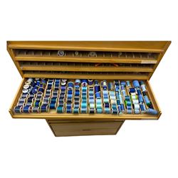 Large beech haberdashery thread storage cabinet, rectangular form with fourteen glass-fronted sloping drawers housing an extensive array of thread spools in assorted colours, over two larger drawers, raised on plinth base