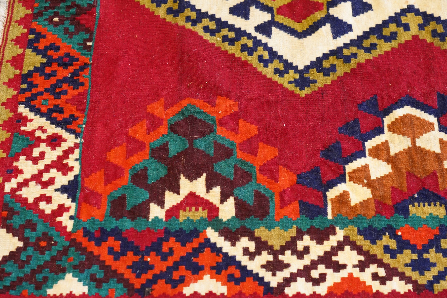 Persian Qashqai crimson ground rug, the central narrow ivory field decorated with repeating hooked geometric lozenges in multicolours, with a densely decorated guard band