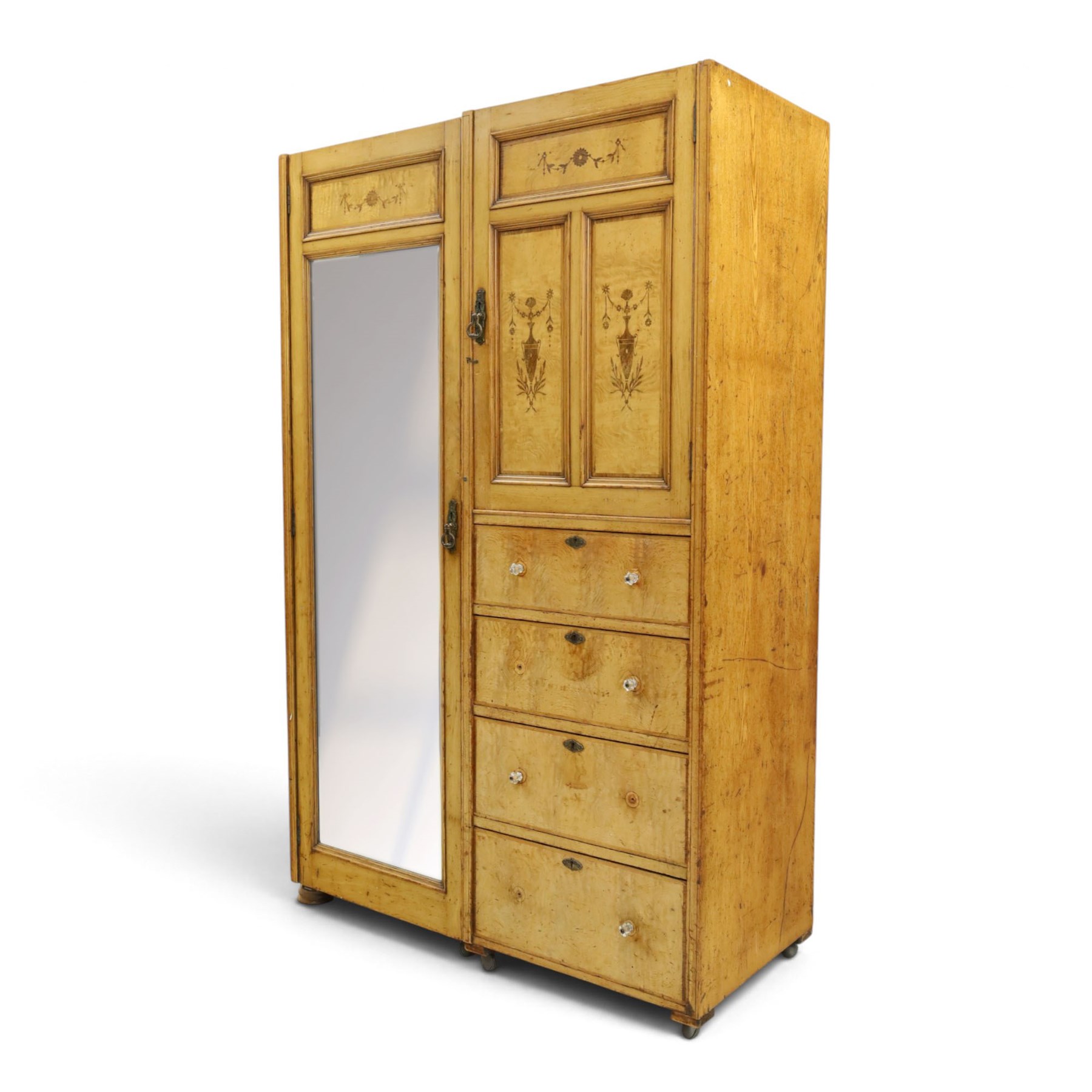 Edwardian Neoclassical figured ash and inlaid double combination wardrobe, the left section with mirrored door enclosing a hanging rail, the right section with cupboard door above four graduated drawers with glass knobs, raised on castors