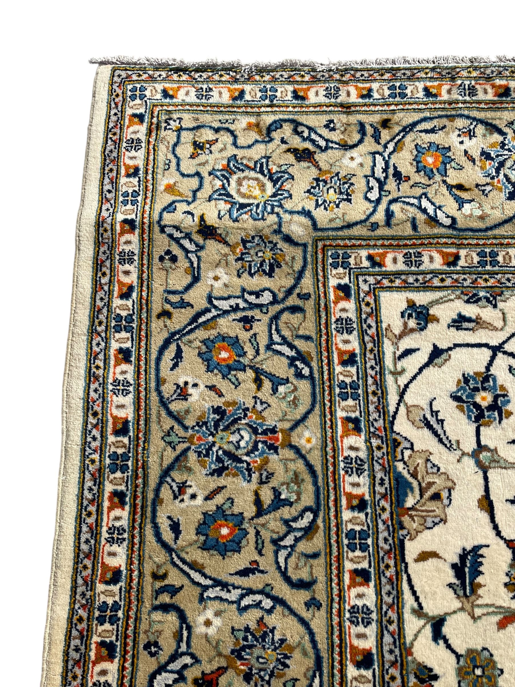 Persian Kashan ivory ground carpet, overall floral design, the field decorated with scrolling and interlaced leafy branches interspersed with palmettes, scrolling border decorated with stylised plant motifs, within floral pattern guard stripes 